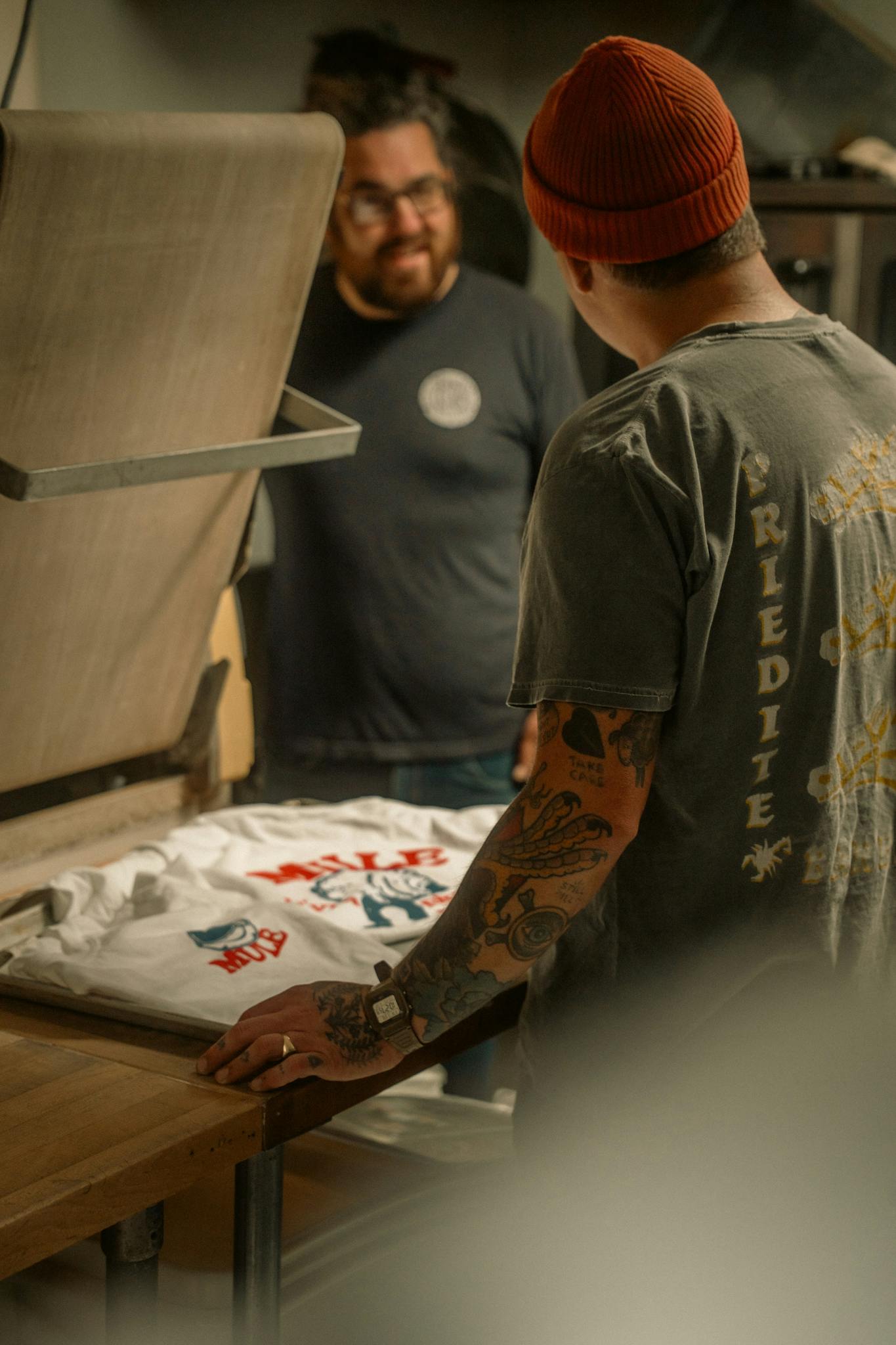 Two men engaged in screen printing a t-shirt in a cozy workshop setting.